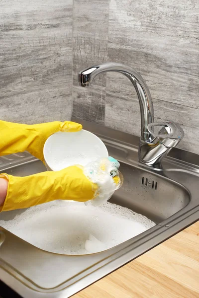 Hands in yellow gloves washing bowl against kitchen sink