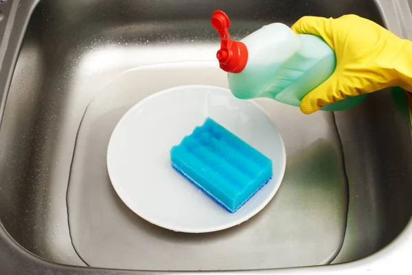 Évier avec eau, plaque, éponge de nettoyage bleue, détergent — Photo