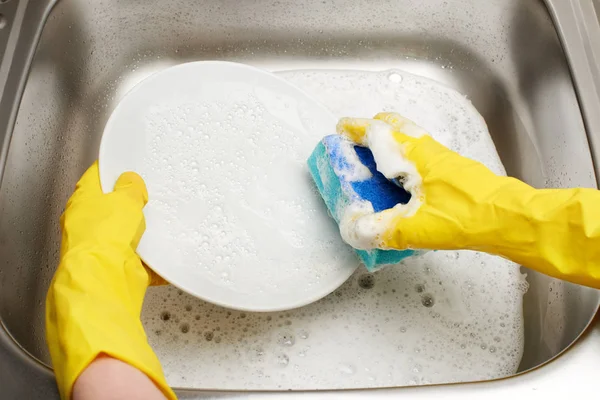 Hands in  gloves washing plate with blue cleaning sponge