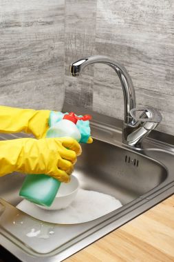Ellerinde eldiven sünger ve deterjan ile yemek takımı yıkama