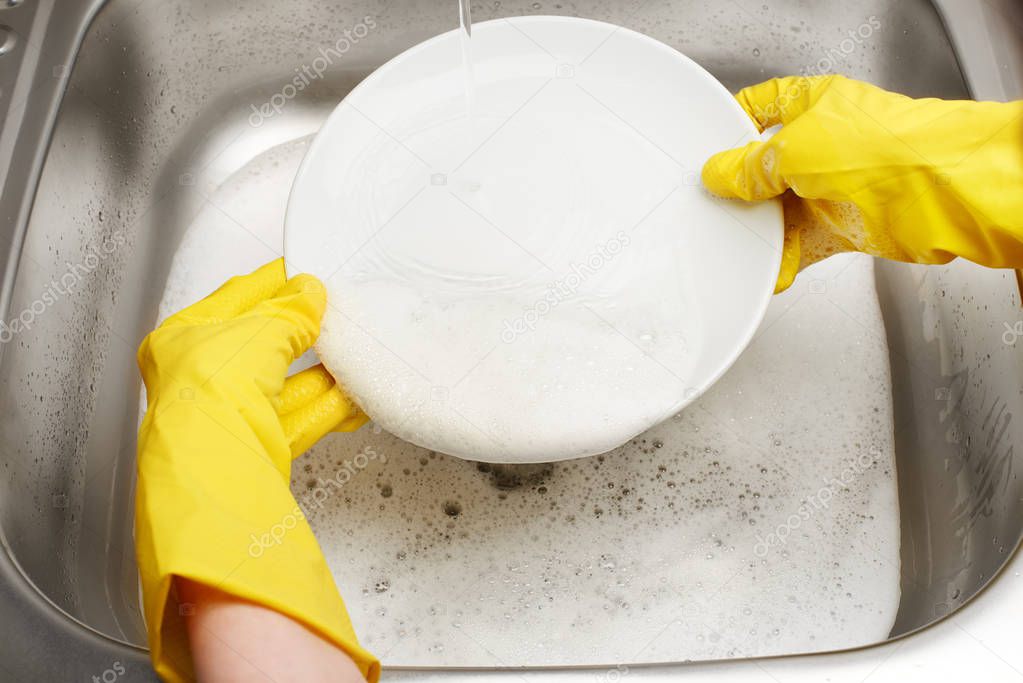 Hands in gloves washing white plate under running tap water 