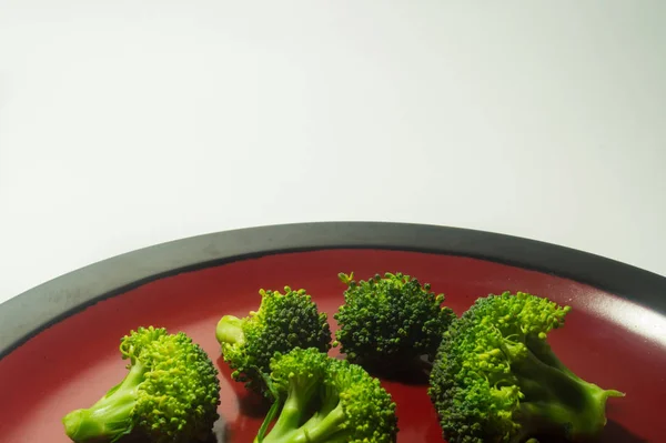 Grüne Brocolli auf rotem und schwarzer Platte auf weißem Hintergrund — Stockfoto