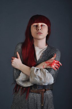 Ortaçağ kız zincirden Kızıl saçlı, gri bir arka plan üzerinde kanla ellerinin üzerinde duruyor
