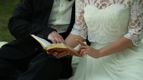 Yong bruden och brudgummen sitter i parken och befria boken — Stockvideo