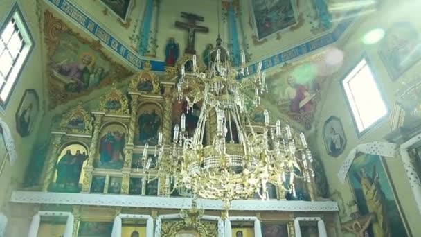 A dim old church interior lit by suns rays penetrating through a colorful stained glass window in the pattern of a crucifix reflecting colors on the floor and a speech pulpit — Stock Video