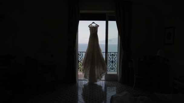 Vestido de noiva pendurado na entrada, fundo ver — Vídeo de Stock