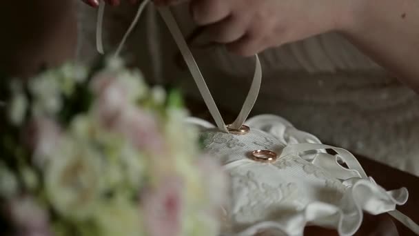 Крупный план руки невесты, которая привязывает обручальные кольца к красивой подушечке — стоковое видео