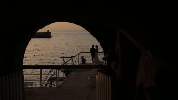 In de boog, de silhouetten van de bruid en bruidegom tegen de achtergrond van de zee — Stockvideo