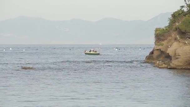 Un pequeño barco navegando a lo largo del mar, en el fondo de una isla con montañas — Vídeo de stock