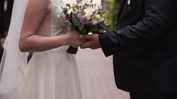 Γάμος, κοντινό πλάνο, νύφη και γαμπρός ενώνουν τα χέρια με ένα γαμήλιο μπουκέτο — Αρχείο Βίντεο