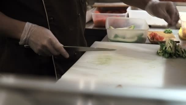 Processo de fazer rolos de sushi. Homem a cortar abacate de rito verde por fatias. Os rolos de sushi preparados passam em primeiro plano — Vídeo de Stock