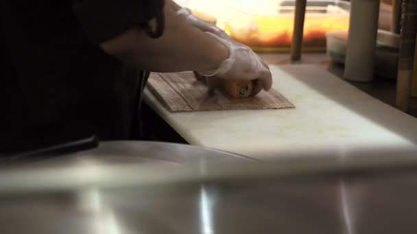 Processo de fabricação e corte de rolos de sushi laranja. Homem rolando up conjunto de sushi usando tapete de bambu. Os rolos de sushi preparados passam em primeiro plano — Vídeo de Stock