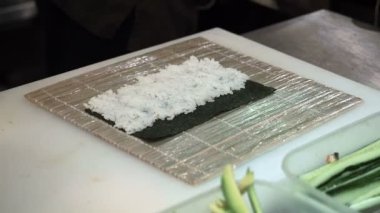 Oluşturma turuncu suşi kesme işlemine alır. Adam bambu hasır kullanarak suşi haddeleme. Hazırlanan suşi rulo tutulur geçmesine