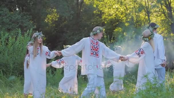 Skupina mladých lidí v slovanských národních krojích tančí v kruhu kolem ohně. Národní slovanských rituálů a tance ve zpomaleném filmu. Letní slunovrat.