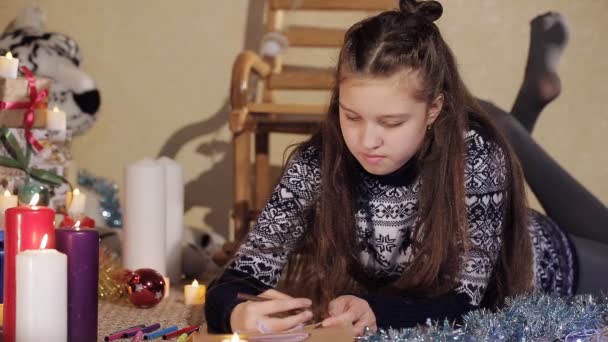 Beautiful girl writes a letter to Santa Claus. A girl with long hair lay on the floor and wrote a letter to Santa Claus. Background with christmas presents.