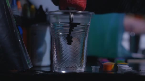 A tattooist mixing ink in a cup of water in a tattoo studio in slow motion