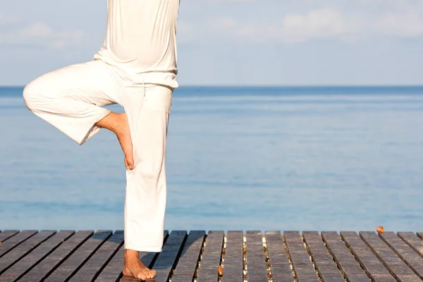 Man in white clothes meditating yoga on wooden pier — Stock Photo, Image