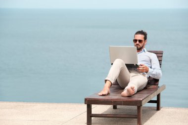 Sahilde dizüstü bilgisayar kullanarak bir takım giyen işadamı