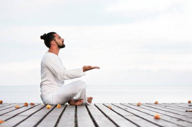 Adam beyaz giysili ahşap iskele yoga meditasyon