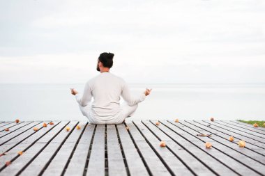 Adam beyaz giysili ahşap iskele platform üzerinde yoga meditasyon
