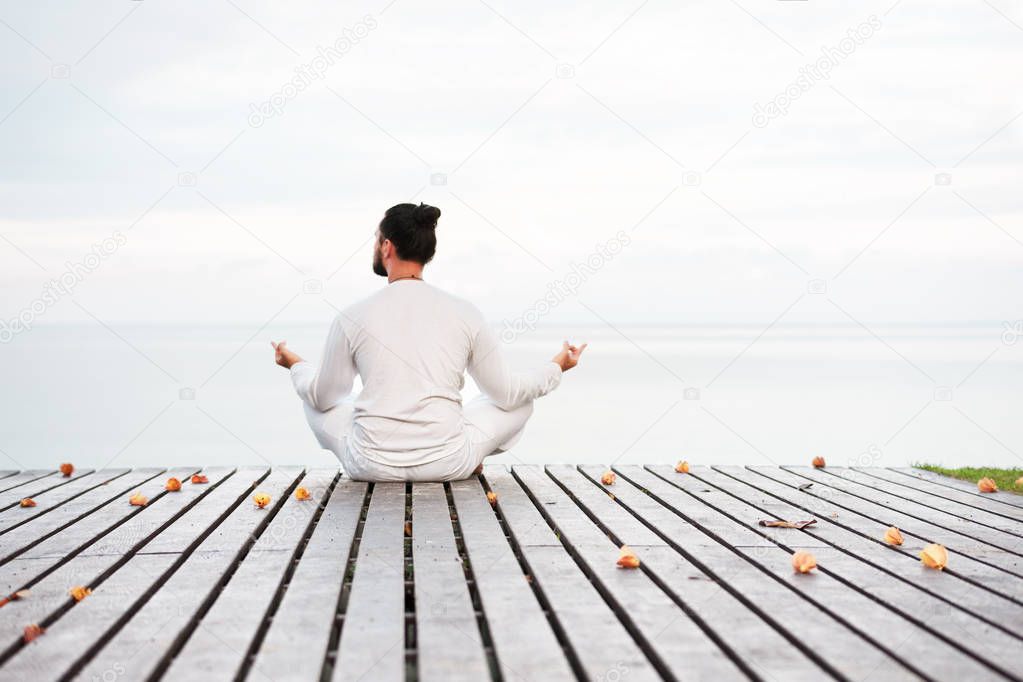 Man in white clothes meditating yoga on wooden pier platform