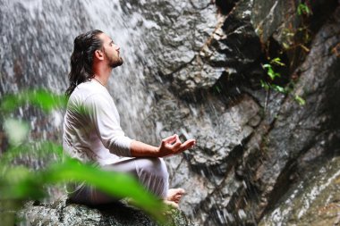 Tropik şelale, meditasyon Yoga kayaya oturan adam