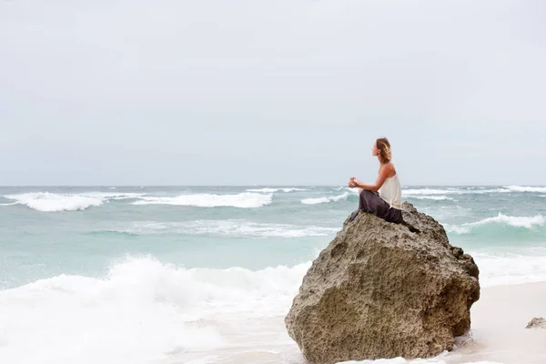 Niña sentada a la orilla del mar en la roca y meditando en pose de yoga —  Fotos de Stock