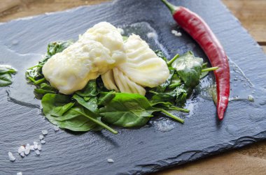 Biber kızarmış ıspanak üzerinde beyaz balık fileto. Gri arka planı.