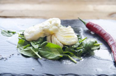 Biber kızarmış ıspanak üzerinde beyaz balık fileto. Gri arka planı.