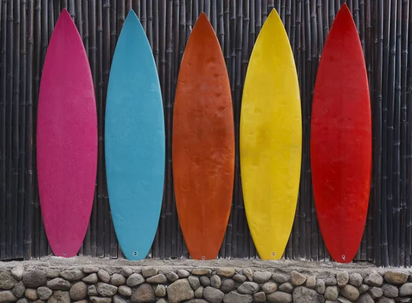 Colored surfboards leaning up against a wooden fence