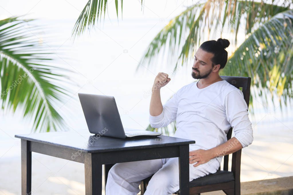 Man relaxing on the beach with laptop, freelancer show win