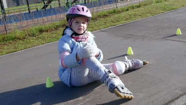 Девушка после несчастного случая сидит на дорожке и массирует колено — стоковое видео