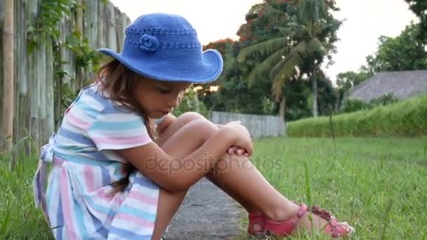 Boldog kis lány ül a fűben, és játszik a nyári kerttel. A szabadban. Naplemente. — Stock videók