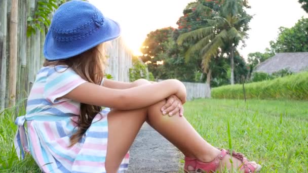 Menina feliz sentada na grama e brincando no jardim de verão. Ao ar livre. Pôr do sol . — Vídeo de Stock