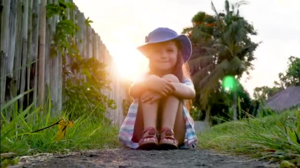 Gelukkig klein meisje zittend op het gras en het spelen in de zomertuin. Buitenshuis. Zonsondergang. — Stockvideo