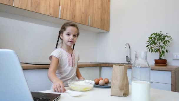Little girl learns to cook in the kitchen and make bakery using laptop — Stock Video