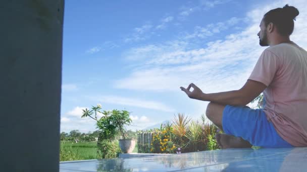 L'homme assis dans le lotus de yoga pose à l'herbe verte dans la prairie et médite . — Video