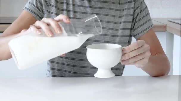 Закройте женскую руку, наливая молоко в чашку на столе — стоковое видео