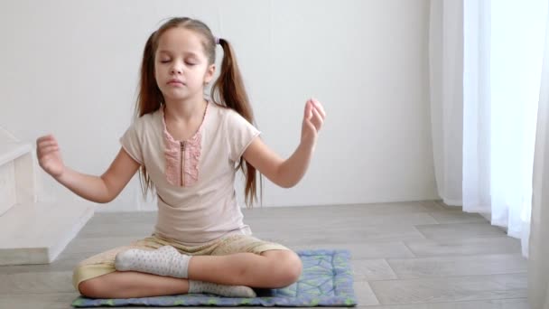 Pequena menina bonito sentado em postura de lótus ioga e medita perto da janela — Vídeo de Stock