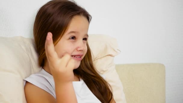 Маленька дівчинка лежить хвора у ліжку. Вона грає з пальцями — стокове відео