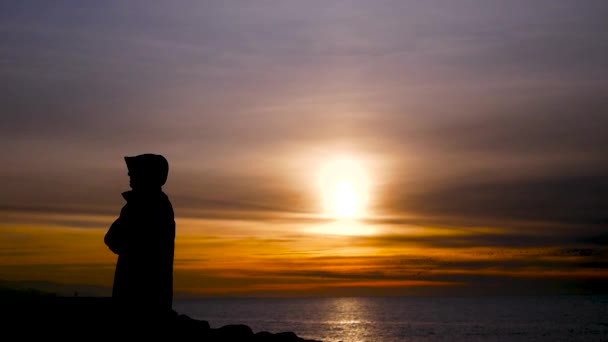 Rückansicht eines Mannes, der auf der felsigen Seebrücke steht und den Sonnenuntergang über dem Meer genießt. slo mo — Stockvideo