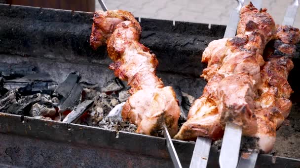 ジューシーなおいしいバーベキューは、グリルの熱い石炭で揚げられています。軸の周りに唾を吐くように回転します。フードフェスティバル揚げジューシーな肉。豚肉は石炭で揚げられる。. — ストック動画
