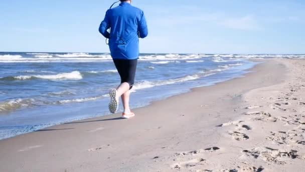 Una donna corre lungo la riva pietrosa dell'oceano. Stile di vita sano e attivo . — Video Stock