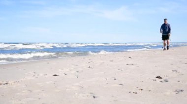 Yaşlı adam, güneşli bir günde İskandinav Sahilinde Yürümek için Çubukları Kullanıyor