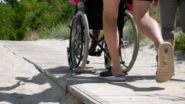 Loisirs en famille. Jeune femme et homme avec sa mère handicapée en fauteuil roulant marchant dans le parc — Video