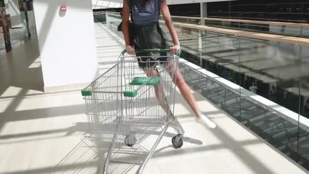 Bella ragazza si diverte a cavalcare sul carrello della spesa al supermercato . — Video Stock
