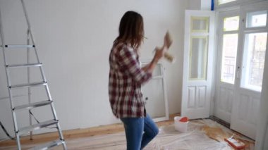 Genç dişi yeni bir dairede onarım yapıyor. Güzel kız. Dairenin duvarını boyuyor. Neşeli ve dans eden komik bir kadın..