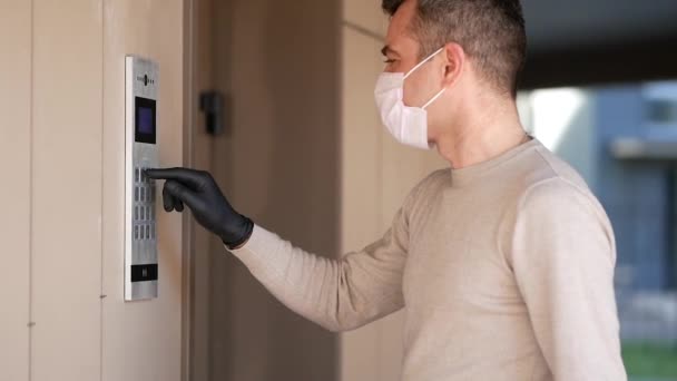 Yüz maskeli ve eldivenli bir adam dahili telefondan kodu çeviriyor ve evinin verandasına giriyor. Salgın Covid-19 konsepti. yavaş çekim — Stok video