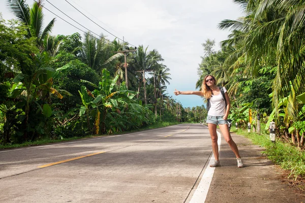 Jovem mulher carona ao longo de uma estrada — Fotografia de Stock