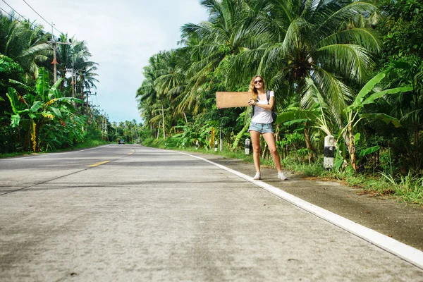 Jovem mulher carona ao longo de uma estrada — Fotografia de Stock